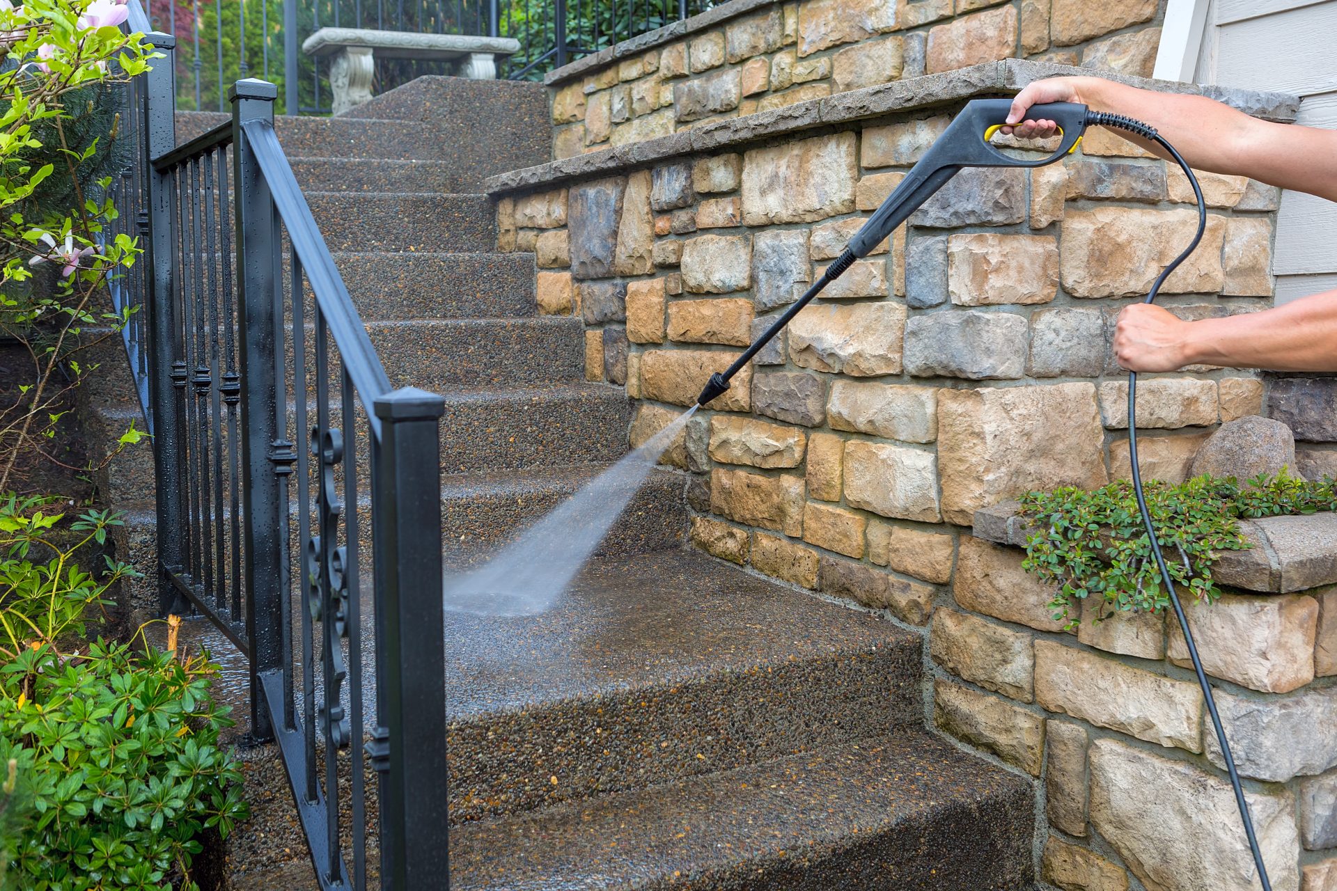 Person pressure washing stone wall and driveway with handheld power washer