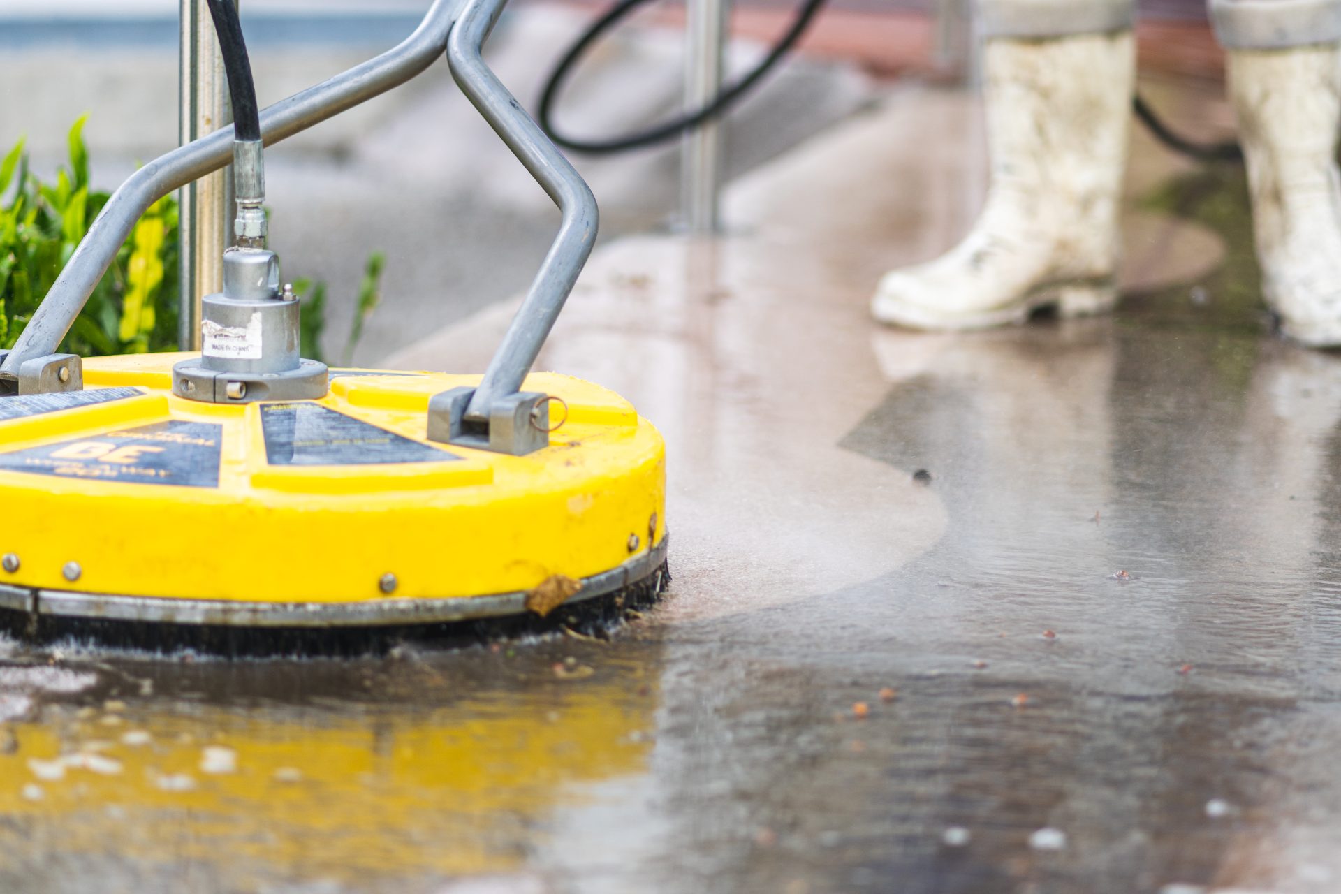 Yellow commercial surface cleaning equipment spraying water on wet pavement